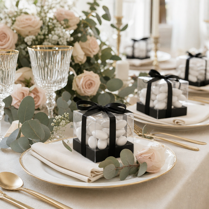 Boîtes cadeaux invités transparentes posées sur les assiettes d'une table de mariage